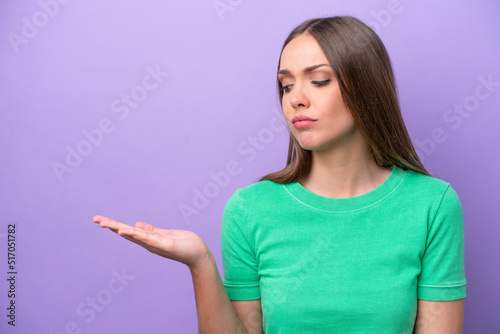 Young caucasian woman isolated on purple background holding copyspace with doubts