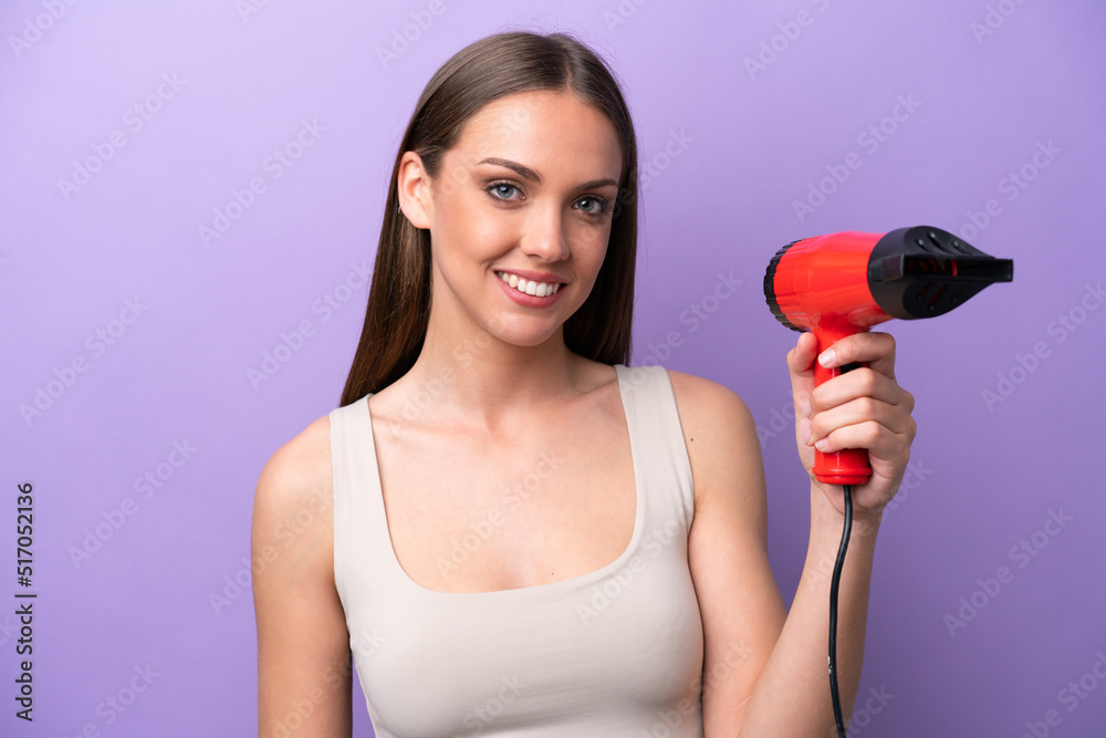 Young caucasian woman holding a hairdryer isolated on purple background smiling a lot Young caucasian woman holding a hairdryer isolated on purple background smiling a lot