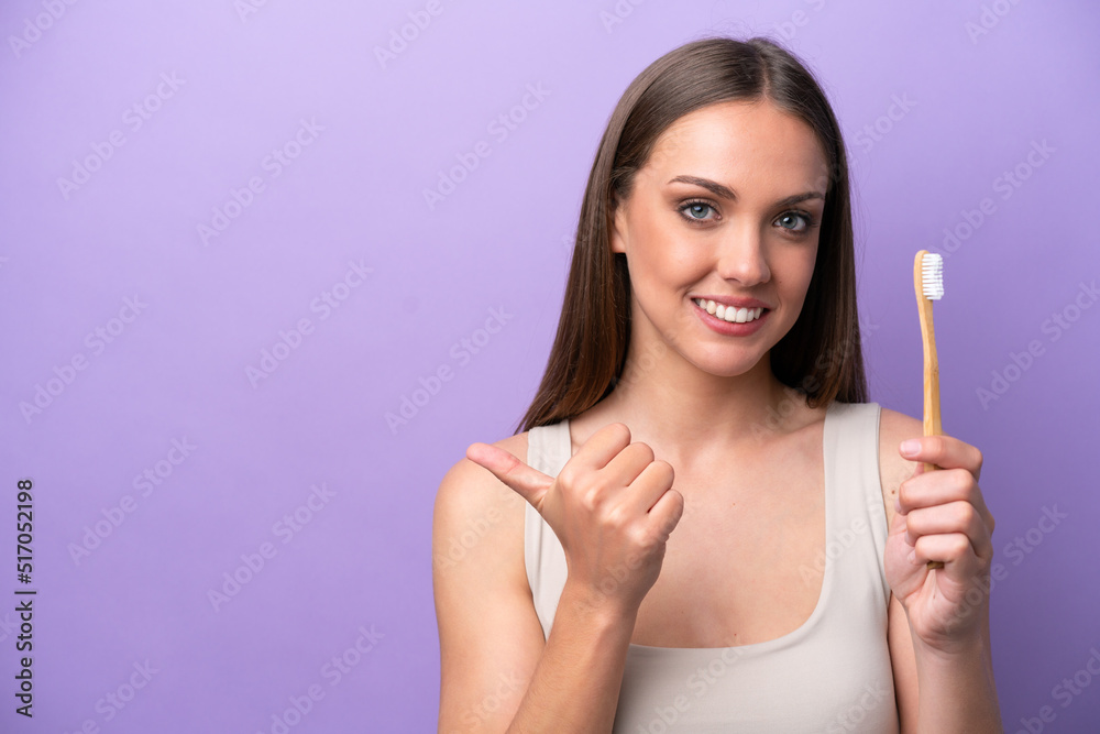 Young caucasian woman brushing teeth isolated on purple background pointing to the side to present a product Young caucasian woman brushing teeth isolated on purple background pointing to the side to present a product
