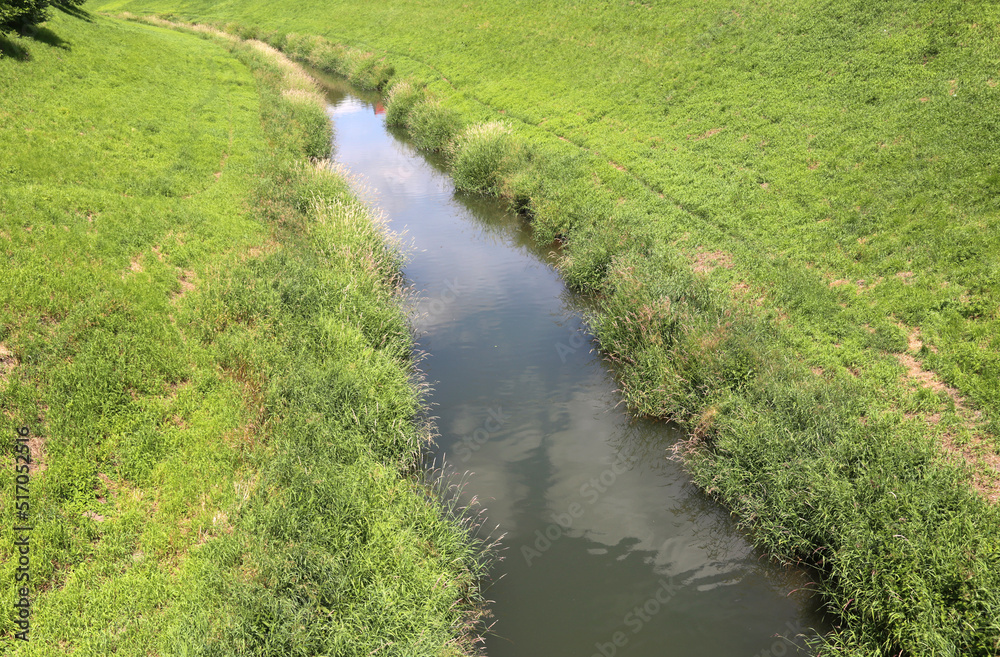 Narrow river flows between grass covered banks.