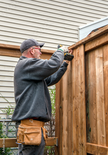 A Caucasian, middle-aged gay male carpenter builds a wooden fence. © Robert