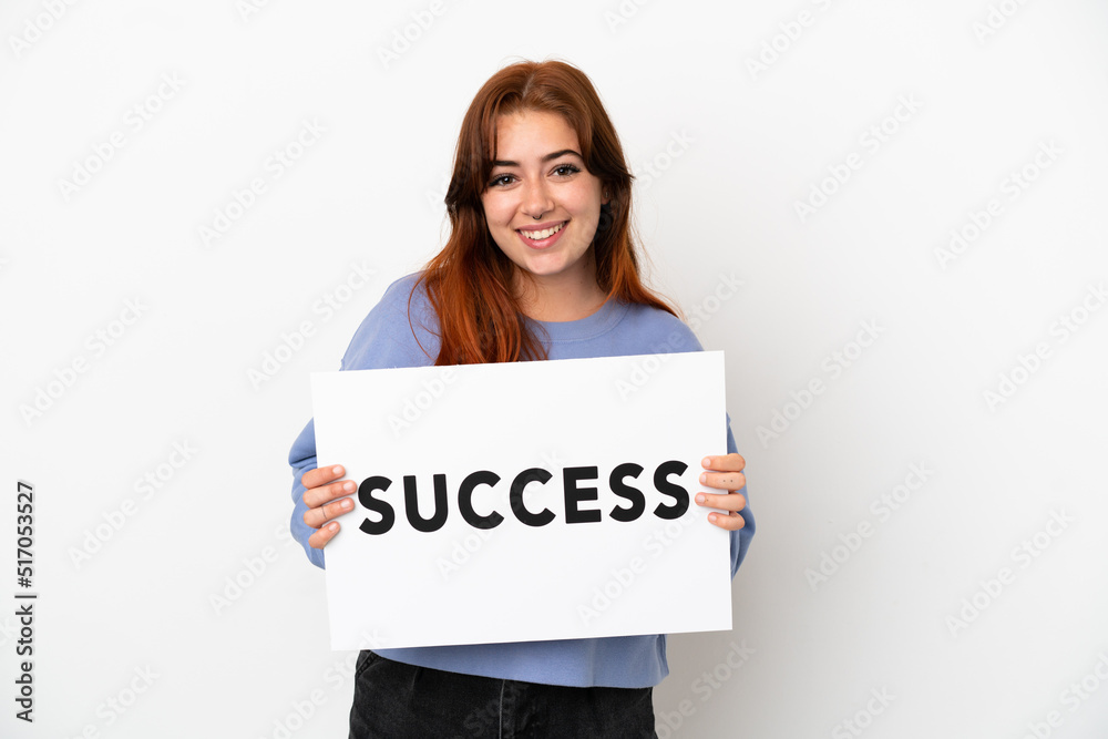 Young redhead woman isolated on white background holding a placard with text SUCCESS with happy expression