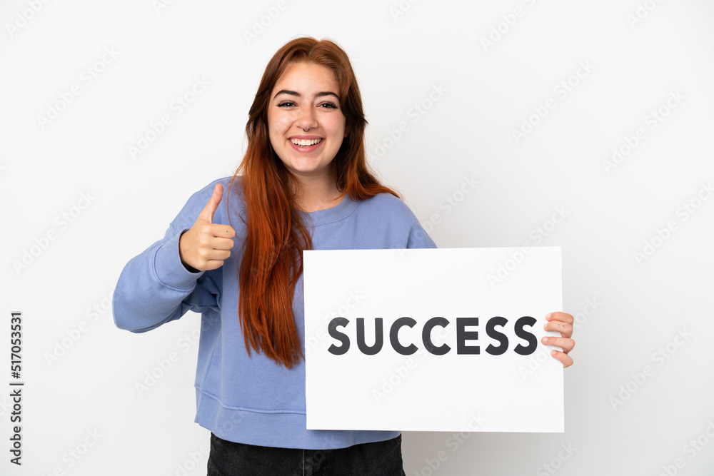 Young redhead woman isolated on white background holding a placard with text SUCCESS with thumb up Young redhead woman isolated on white background holding a placard with text SUCCESS with thumb up