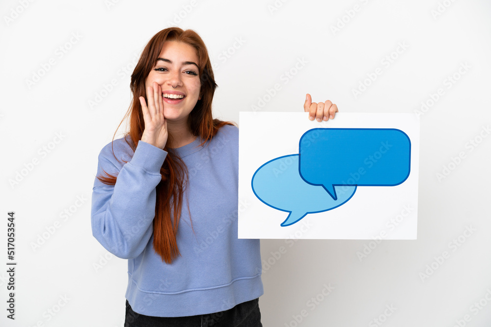 Young redhead woman isolated on white background holding a placard with speech bubble icon and shouting Young redhead woman isolated on white background holding a placard with speech bubble icon and shouting