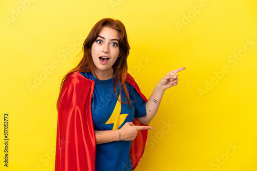Super Hero redhead woman isolated on yellow background surprised and pointing side