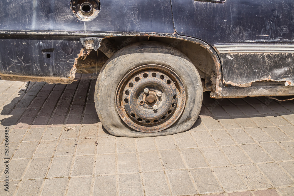 A flat old tire on a rusty rotten car