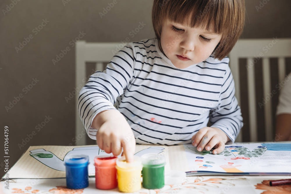 Finger painting. Portrait of cute little boy painting with fingers at home. Close-up of child's hand in colorful paints. Early education concept. Sensory play. Development of fine motor skills. Finger painting. Portrait of cute little boy painting with fingers at home. Close-up of child's hand in colorful paints. Early education concept. Sensory play. Development of fine motor skills.