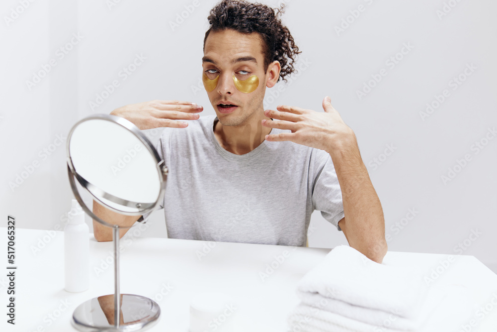 guy with curly hair in a white T-shirt sits at a table with a mirror and a towel face patches light background guy with curly hair in a white T-shirt sits at a table with a mirror and a towel face patches light background