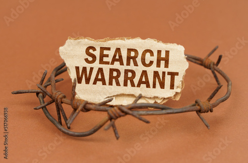 On a brown surface, barbed wire and a cardboard sign with the inscription - Search warrant photo