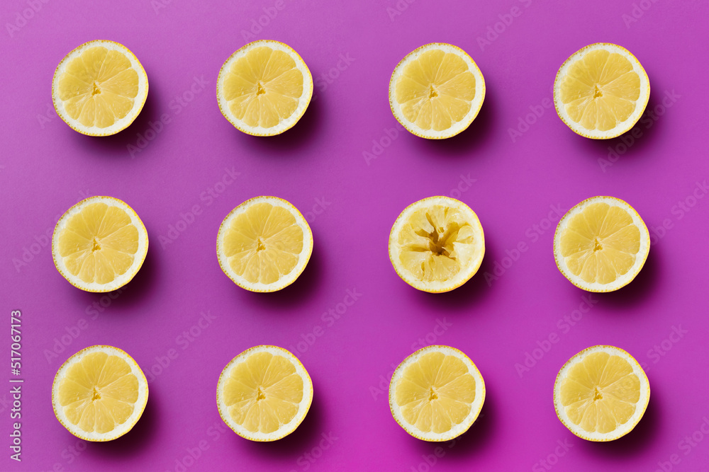 Twelve yellow sour half lemons on light purple background, one half is pressed