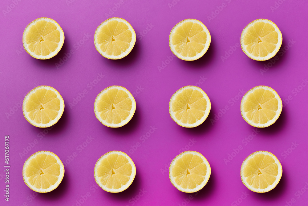 Twelve yellow sour half lemons on light purple background