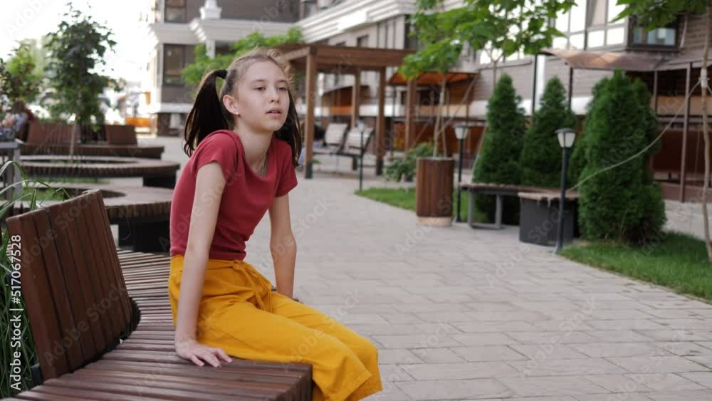 The girl preteen is sitting on a bench in the courtyard of the neighborhood and is sad. A lonely girl is sad on a bench. The girl preteen is sitting on a bench in the courtyard of the neighborhood and is sad. A lonely girl is sad on a bench.