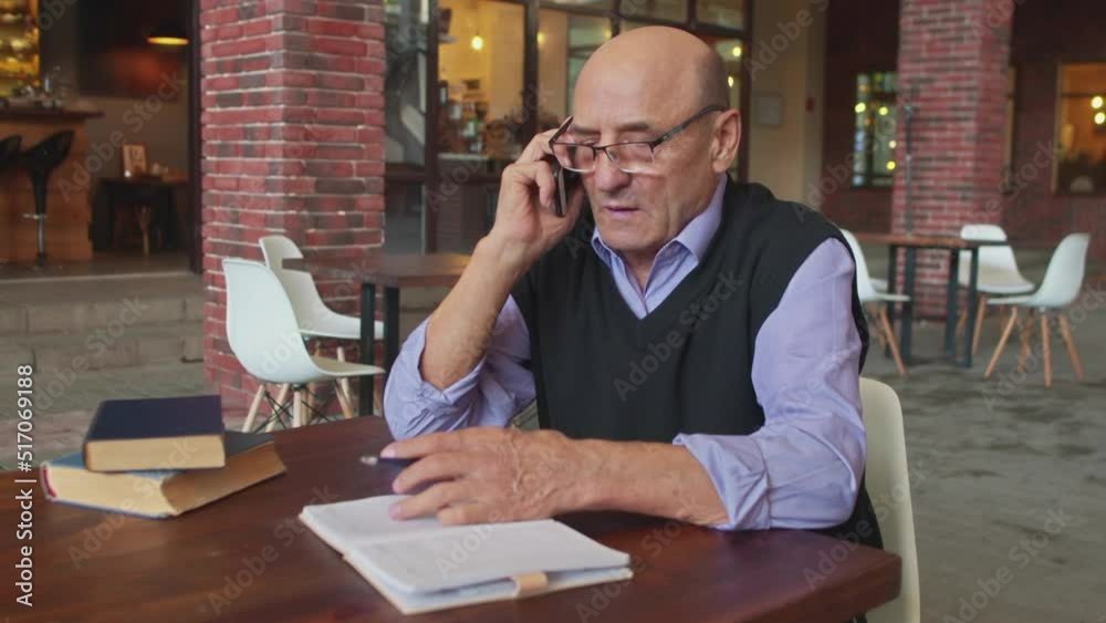 Senior man talks on phone and makes note in notebook in cafe Senior man talks on phone and makes note in notebook in cafe
