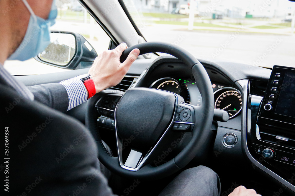 young man driver in a medical mask and business suit driving a new car