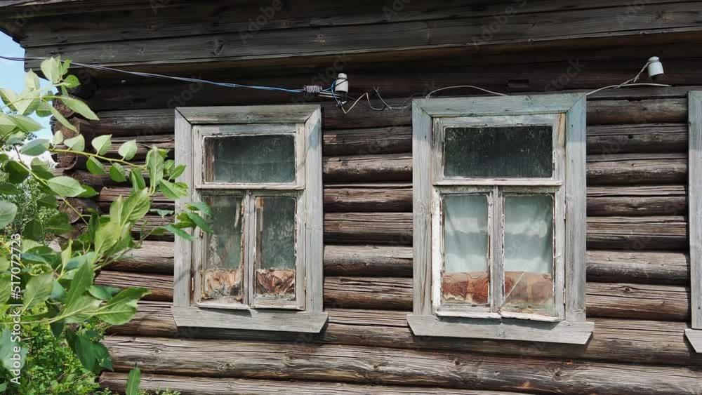 view of an old wooden village house. two broken glass windows. tree branch with green leaves view of an old wooden village house. two broken glass windows. tree branch with green leaves