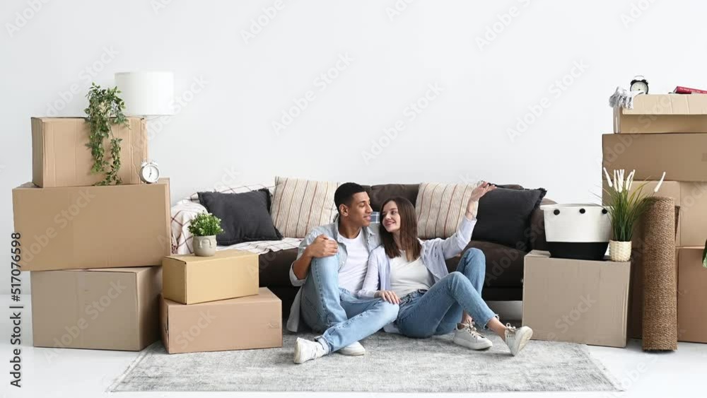 Happy young multiracial couple, caucasian woman and hispanic guy, are sitting on the floor between boxes of stuff in their new home or rental apartment, planning their house future design, smile Happy young multiracial couple, caucasian woman and hispanic guy, are sitting on the floor between boxes of stuff in their new home or rental apartment, planning their house future design, smile