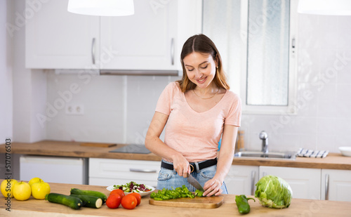 Positive woman is cutting vegetables for salad in the kitchen at home