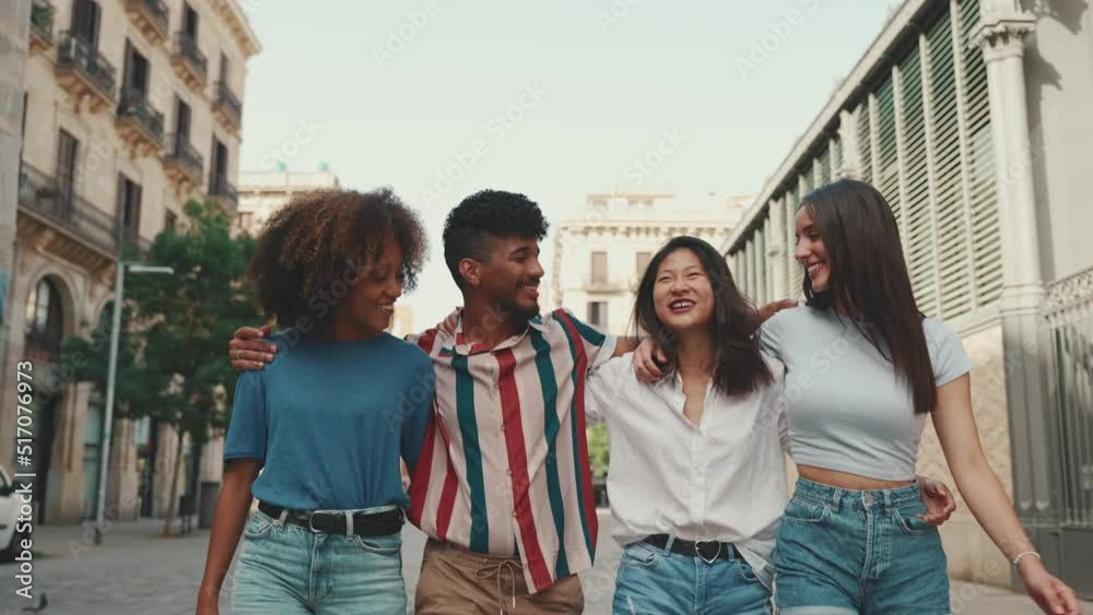 Happy multiethnic young people walk embracing on summer day outdoors. Group of friends are talking and laughing merrily while walking along on the street Happy multiethnic young people walk embracing on summer day outdoors. Group of friends are talking and laughing merrily while walking along on the street