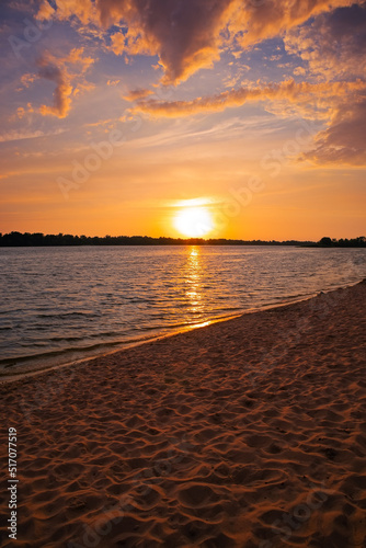 Beautiful sunset over the river  lake  pond . Beach and sand. The sun goes below the horizon. Clouds in the sky. Orange and blue colors