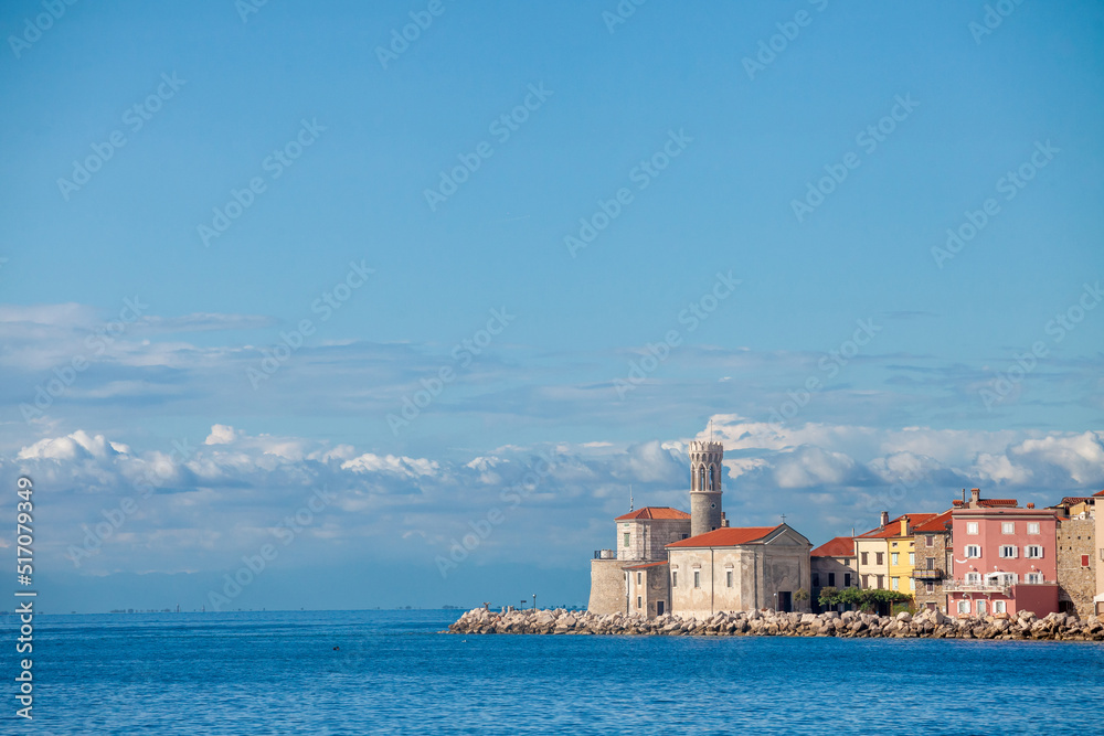 Panorama of  Piran, Slovenia, with Adriatic sea in front, with blue water and sky, on a wharf quay, during a sunny summer afternoon. Piran, or Pirano, is a slovenian city on the adriatic sea in istria