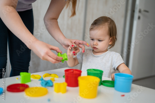 One girl small caucasian toddler child playing with colorful plasticine on the table at home with her mother woman childhood and growing up development concept copy space