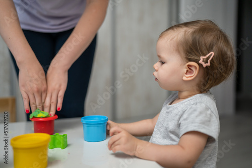 One girl small caucasian toddler child playing with colorful plasticine on the table at home with her mother woman childhood and growing up development concept copy space side view