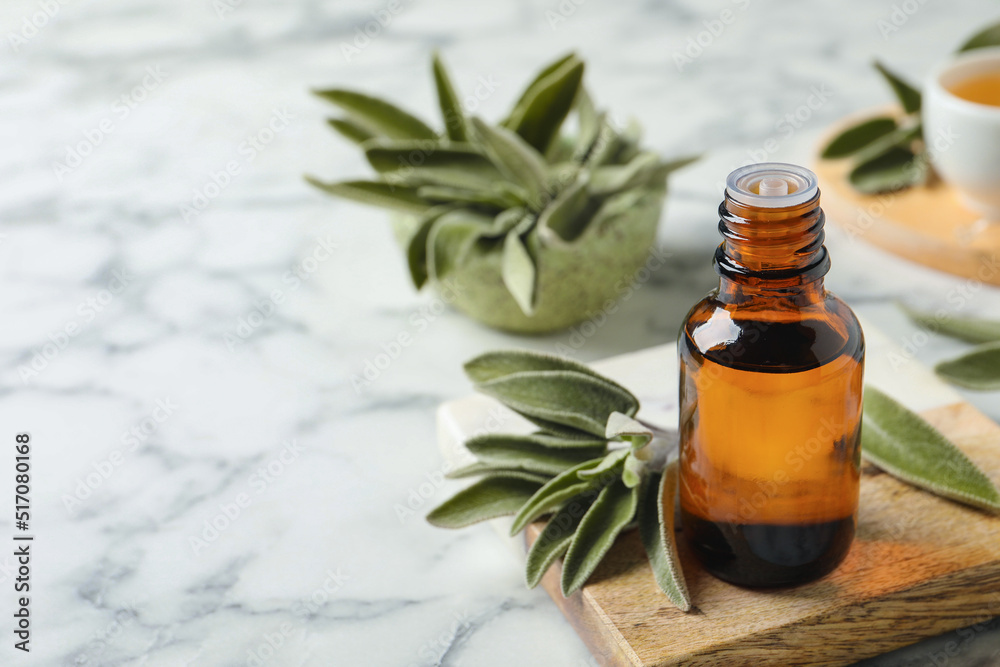Bottle of essential sage oil and leaves on white marble table. Space for text Bottle of essential sage oil and leaves on white marble table. Space for text