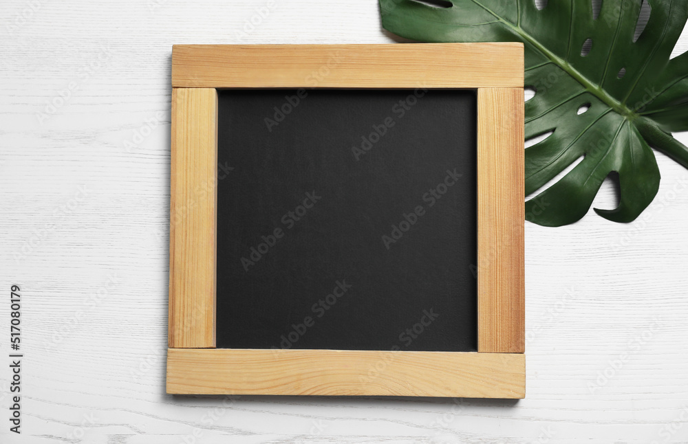 Blank chalkboard with green leaf on white wooden background, flat lay. Space for text