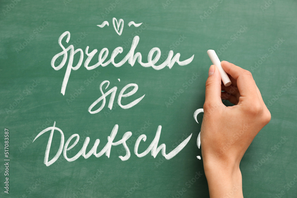 Woman's hand with chalk writing text SPRECHEN SIE DEUTSCH? (DO YOU SPEAK GERMAN?) on blackboard Woman's hand with chalk writing text SPRECHEN SIE DEUTSCH? (DO YOU SPEAK GERMAN?) on blackboard