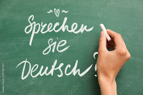 Woman's hand with chalk writing text SPRECHEN SIE DEUTSCH? (DO YOU SPEAK GERMAN?) on blackboard