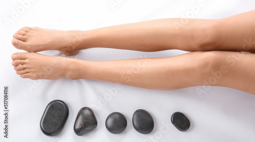 Legs of young woman and spa stones on white background, top view