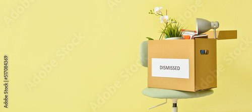 Box with personal stuff and word DISMISSED on chair against yellow background with space for text photo