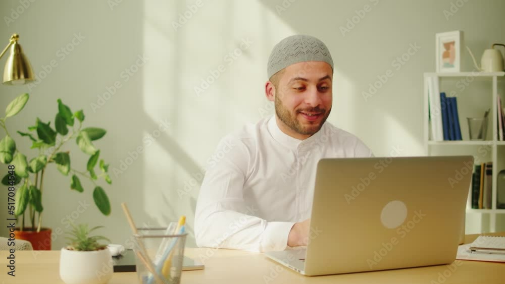 Middle eastern man calling on virtual conference, using laptop. Male person talking on video call. Wearing traditional Islamic clothes. Communicating with family and friends online. Middle eastern man calling on virtual conference, using laptop. Male person talking on video call. Wearing traditional Islamic clothes. Communicating with family and friends online.