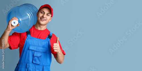 Slika na platnu Delivery man holding bottle of water and showing thumb-up on blue background wit