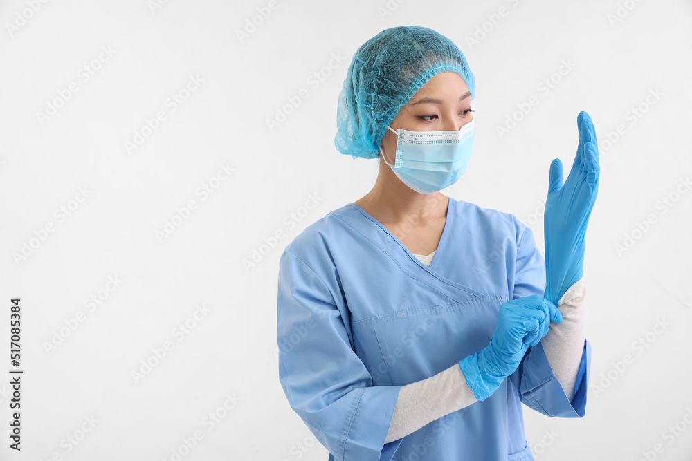 Asian nurse in medical mask putting on rubber gloves against white background Asian nurse in medical mask putting on rubber gloves against white background