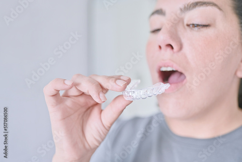 Orthodontic teeth corrector. Young woman prepares by opening her mouth to place an invisible brace made of silicone to align her teeth. Oral health.