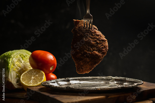 beef or chicken milanese in breadcrumbs with lettuce and tomato on a dark background