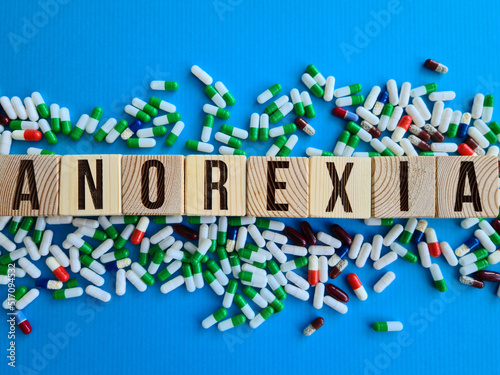 Word anorexia made from wooden cubes with letters next to pills on blue background photo