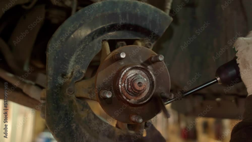 An auto mechanic cleans a spacer on a car hub with a metal brush, dressed on a drill, before replacing the brake disc of a car wheel of a raised car at a repair station. 4k An auto mechanic cleans a spacer on a car hub with a metal brush, dressed on a drill, before replacing the brake disc of a car wheel of a raised car at a repair station. 4k