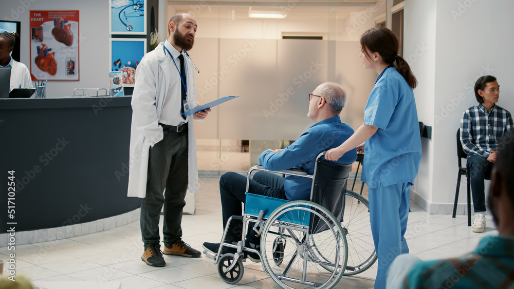 Male doctor meeting with old patient in wheelchair at reception lobby, having conversation about healthcare and support. Man with chronic disability having checkup visit with specialist. Male doctor meeting with old patient in wheelchair at reception lobby, having conversation about healthcare and support. Man with chronic disability having checkup visit with specialist.