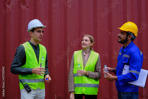Three Caucasian workers in the freight industry in container background, take a break and relaxing from logistics work exhaust by drinking water, resting, cargo shipping transportation business.