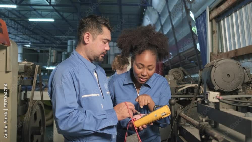 Asian male and female African American engineers in safety uniform work by inspecting machines' voltage current, checking, and maintaining at manufacture factory, electric system service occupations. Asian male and female African American engineers in safety uniform work by inspecting machines' voltage current, checking, and maintaining at manufacture factory, electric system service occupations.