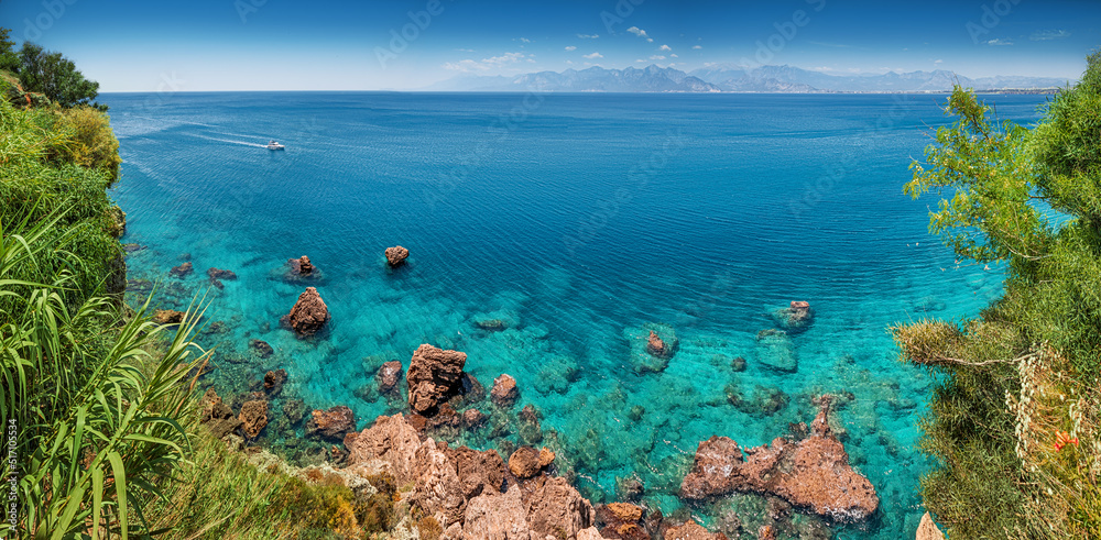 Aerial scenic panoramic seascape view from a high cliff. Vacation background and coastline concept. Azure sea bottom and sailing motor boat on a transparent waters