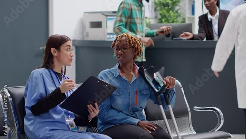 African american woman with crutches suffering from physical impairment, talking to medical assistant abour disability and recovery. Diverse people discussing in hospital reception area. photo