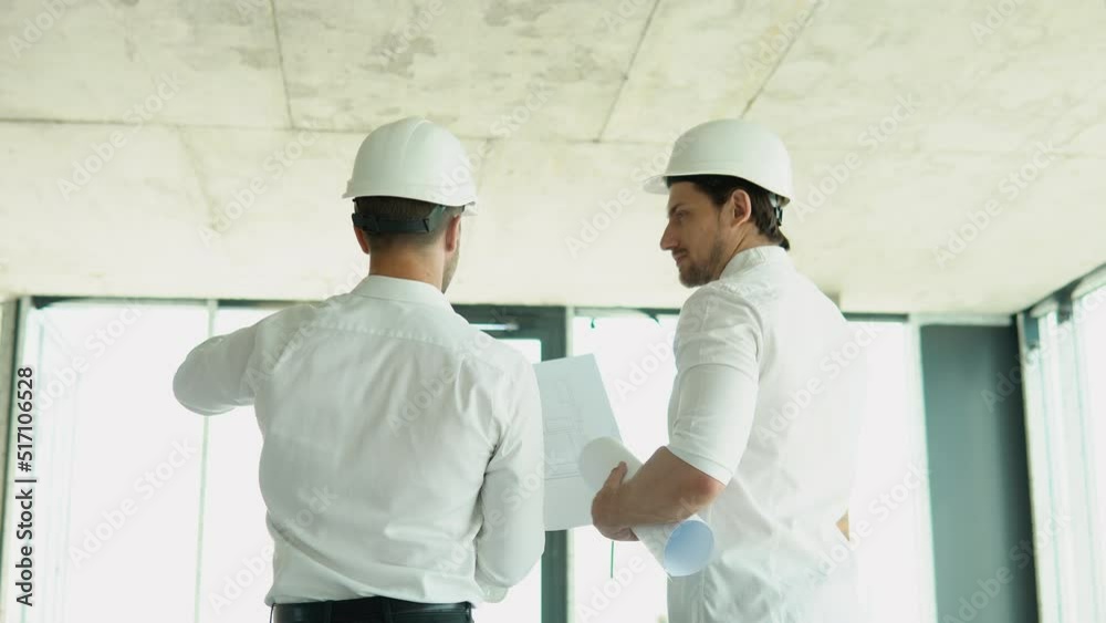 Two men in helmet look at the plan of the building Two men in helmet look at the plan of the building