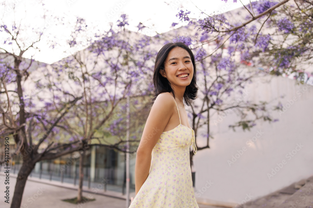 Attractive brunette young woman staying in the park in the city . Fair-skinned asian lady look with smile at camera wearing yellow dress. Relaxing, street style concept Attractive brunette young woman staying in the park in the city . Fair-skinned asian lady look with smile at camera wearing yellow dress. Relaxing, street style concept