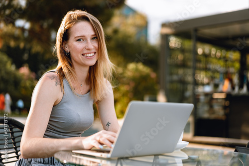 Happy beautiful young woman working on laptop in street cafe