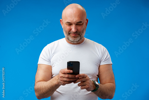 Happy middle-aged man with a phone in his hands against blue background