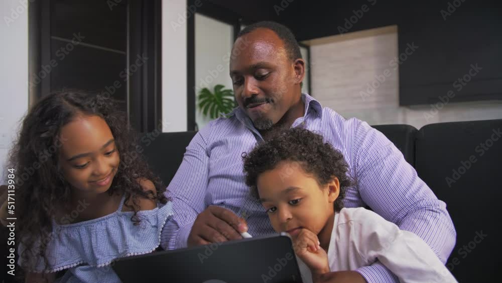 African american man and his childrens drawing on a tablet sitting on the couch at home.Dad shows how he draws.Slow Motion.Close-up African american man and his childrens drawing on a tablet sitting on the couch at home.Dad shows how he draws.Slow Motion.Close-up