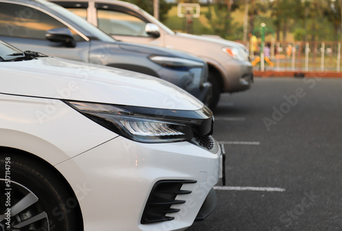 Closeup of front side of white car with other cars parking in outdoor parking area. in twilight evening. © Amphon